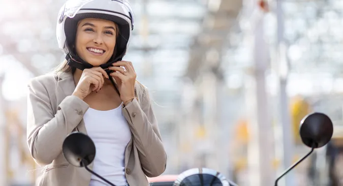 Junge Frau schließt vor Fahrtantritt mit ihrem Roller den Verschluss des Helmes