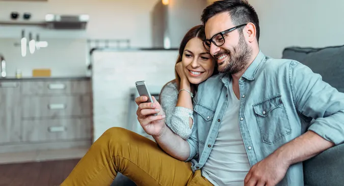 Junges Paar schaut auf dem Smartphone nach geeigneten Einrichtungsgegenständen für ihr erstes gemeinsames Zuhause