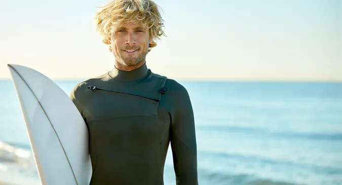 Junger Mann mit Surfbrett unter dem Arm steht am Strand