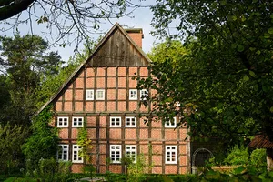 Ein sehr gut erhaltenes Fachwerkhaus aus rotem Backstein steht inmitten einer grünen Oase aus Eichen und Sträuchern
