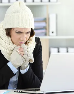 Obwohl die junge Frau mit Mütze, Schal und Handschuhen bekleidet ist, hilft das nicht gegen die frostigen Temperaturen im Büro