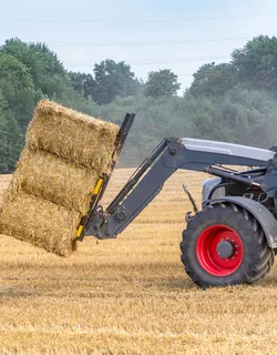 Traktor transportiert Strohballen übers Feld