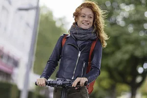 Junge Frau fährt ohne Helm auf einem E-Scooter durch die morgendliche Frische an einem Herbsttag