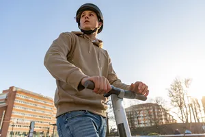 Junger Mann mit Helm ist mit seinem E-Scooter auf dem Weg zum Treffen mit Freunden