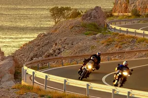zwei Motorräder gleiten über eine kurvige Straße an der Küste entlang