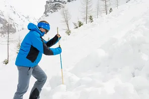 Mann im blauen Windbreaker sticht eine Markierungsstange in den Schnee