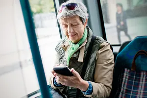 Seniorin sitzt im Bus und wirft einen prüfenden Blick in ihr Smartphone