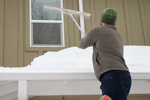 Mann holt mit einer Holzharke die Schneemassen vom Dach des Carports
