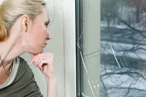 Frau begutachtet frustriert die gesprungene Fensterscheibe