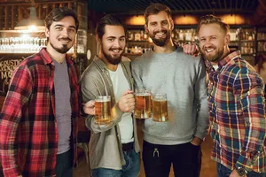 Vier junge Männer prosten ausgelassen mit ihrem Bier in die Kamera