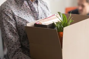 Junge Frau trägt ihre letzten Büro-Habseligkeiten in einem Karton nach Hause