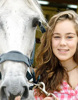 Selfie mit Pferd: Junge Frau lächelt Kopf an Kopf mit ihrem Schimmel in die Kamera