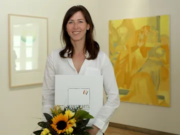 Katharina Neuweg mit Urkunde und Blumenstrauss vor ihren Werken