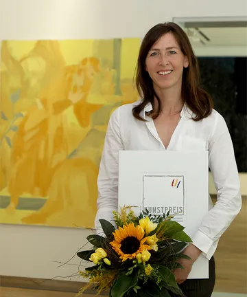 Katharina Neuweg mit Urkunde und Blumenstrauß vor ihren Werken.