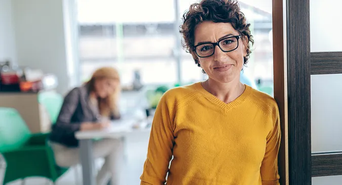 Junge Frau in gelbem Pulli guckt gut gelaunt durch eine schwarzgerahmte Brille
