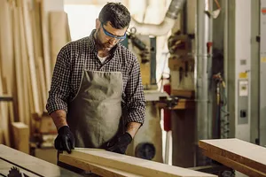 mit Lederschürze und Schutzbrille bekleidet legt sich der Schreinermeister seine Holzlatten zur Verarbeitung zurecht