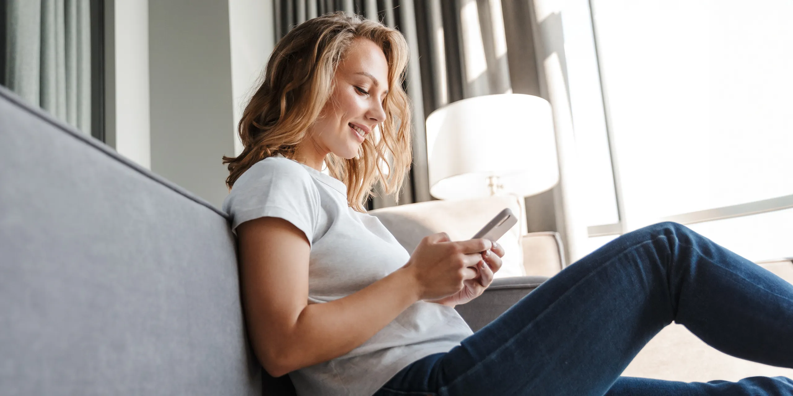 Frau mit Handy sitz auf dem Boden ans Sofa gelehnt